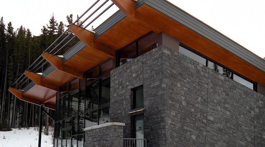 A corner shot of the exterior of the Sulphur Slopes Visitors Pavilion featuring it's stone exterior and mass timber roof.