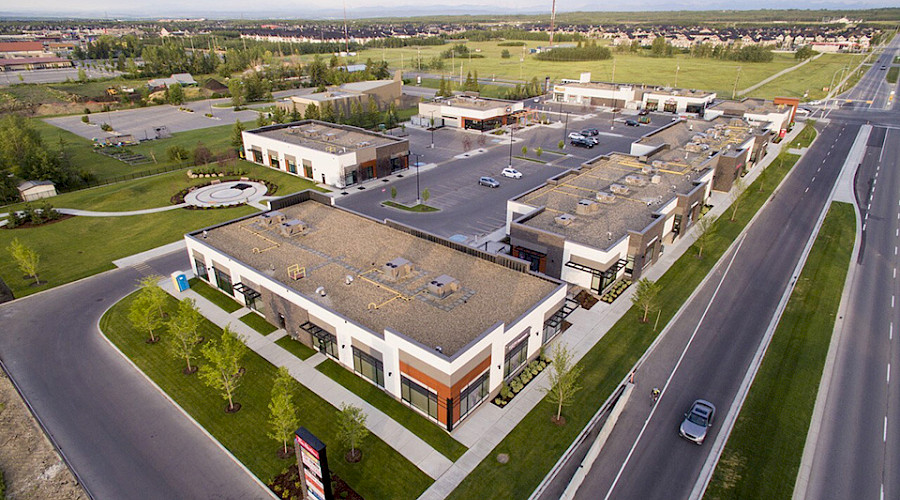 An aerial shot of the Springbank Retail building in between a field of green grass and a road.