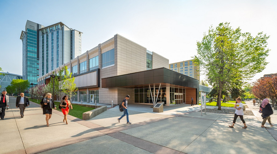 A photo of people walking by the exterior of the John Ware building on a bright day.