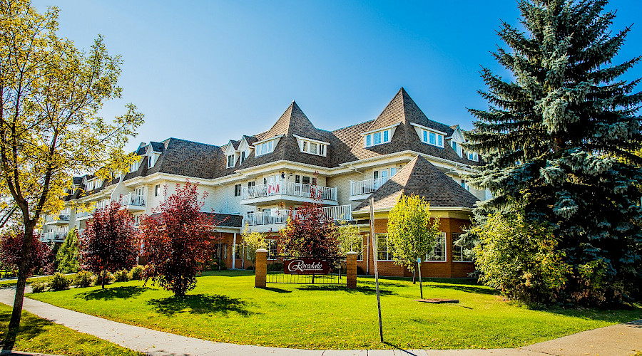 A photo of the exterior of the Rosedale Senior Centre behind trees and a large lawn.