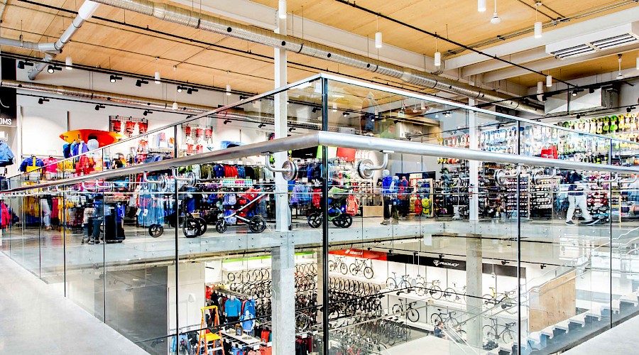 A railing surrounded by glass on the second floor of the MEC store filled with products.