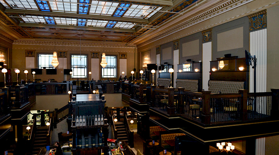 The second floor of a restaurant with large skylights on the ceiling looking down onto a bar top.