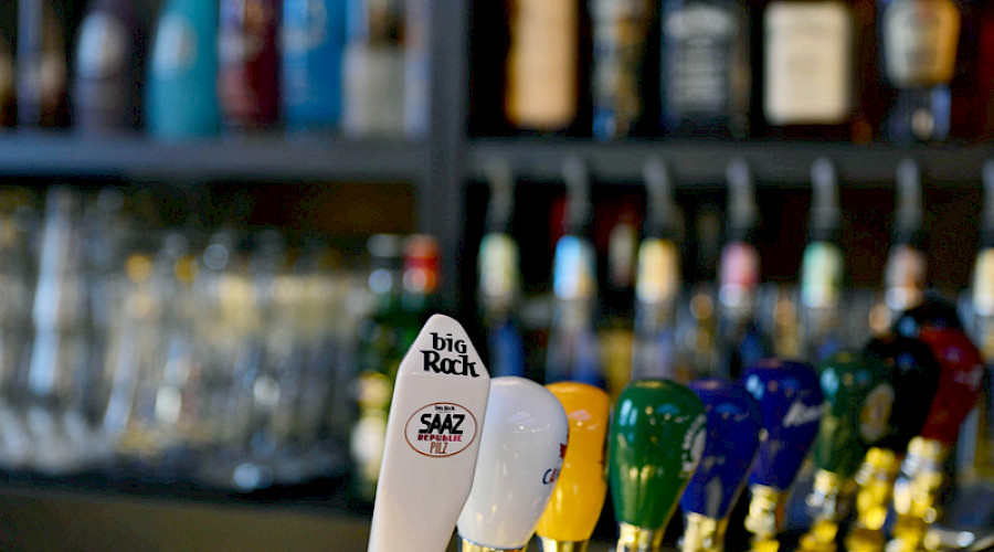 A beer tap in front of shelves of bottles of wines and liquors.