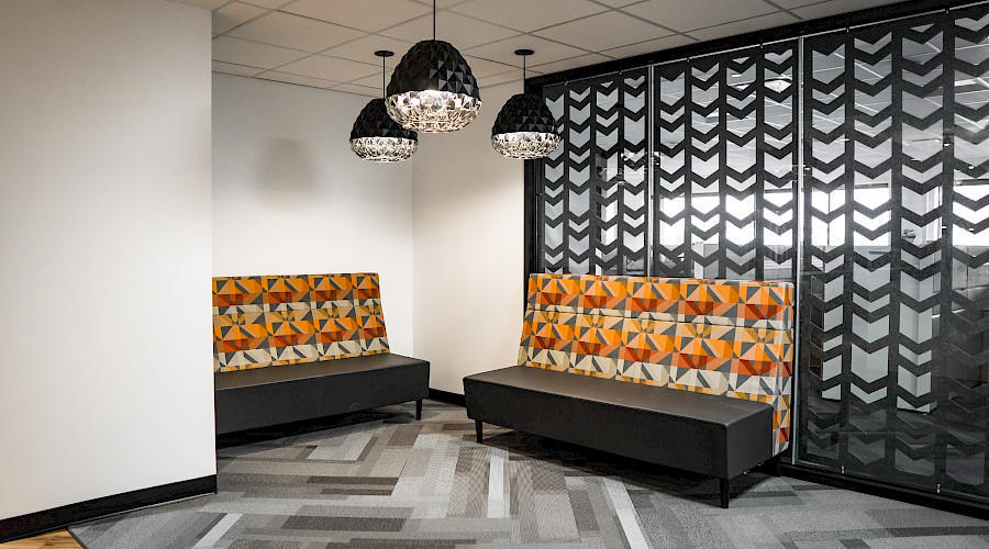 Two orange patterned sofas in corner with three light fixtures hanging above and a grey accent wall behind them.