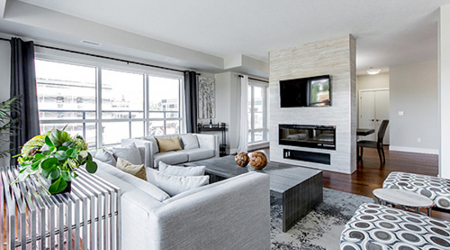 A bright living room with a large grey sectional and a white brick fireplace.