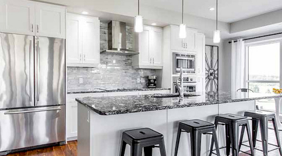 A white and grey kitchen with a stainless steel fridge and long island with four stools.