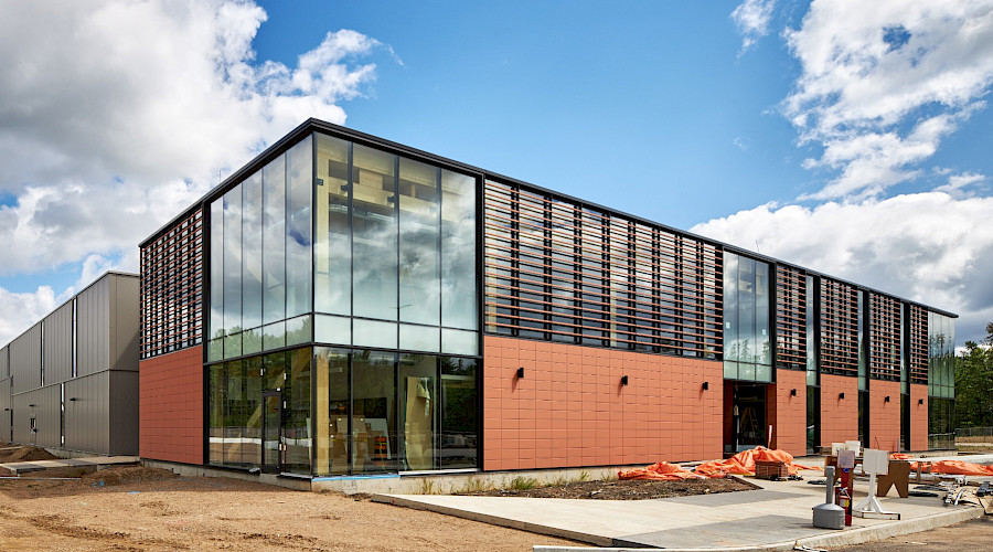 The exterior of the Canadian Nuclear Laboratories building with a cloudy, blue sky in the background, highlighting the building's floor-to-ceiling windows and red brick exterior.