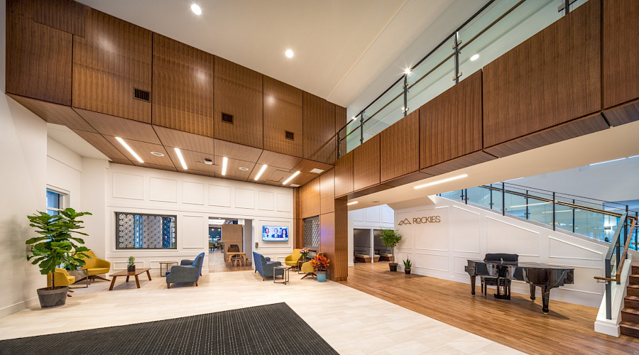 A photo of a large lobby with wood paneling, seating areas and a piano in front of a staircase.