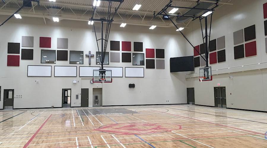 A lit up gymnasium with two basketball hoops.