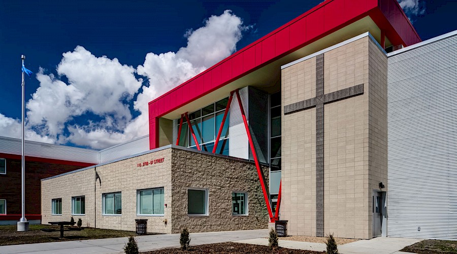 The exterior of St. Joseph High School, featuring a large cross on the stone wall with a deep blue cloudy sky in the background.