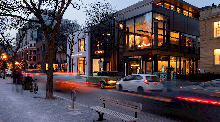 Streaks of red light from cars driving on a road in front of the Yorkville Avenue retail building in the evening.