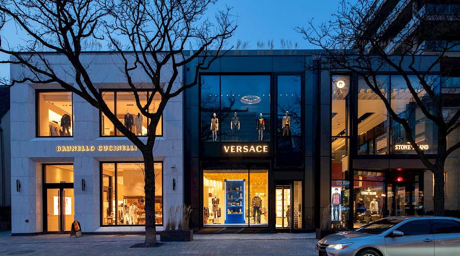 The exterior of the Yorkville Avenue retail building occupied by designer stores that are lit up inside in the evening.
