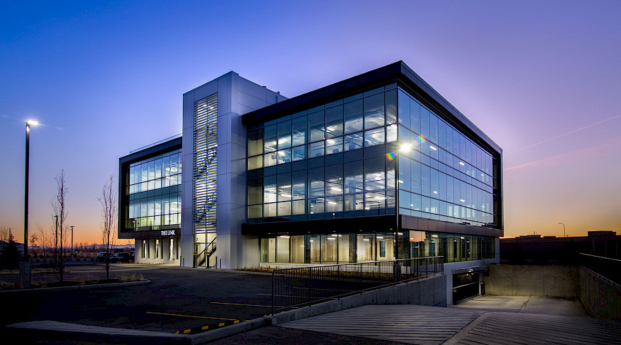 The exterior of the Royal Vista Link building lit up at night, highlighting its' large glass windows.