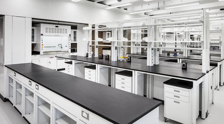 A photo of a clean laboratory classroom with white desks and black countertops.
