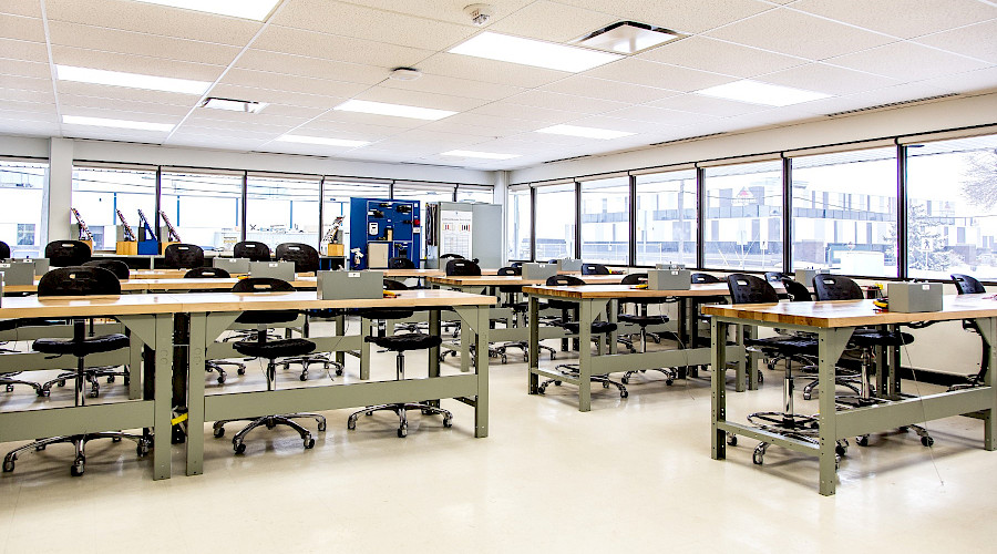 Rows of chairs and desks in a bright classroom with large windows.