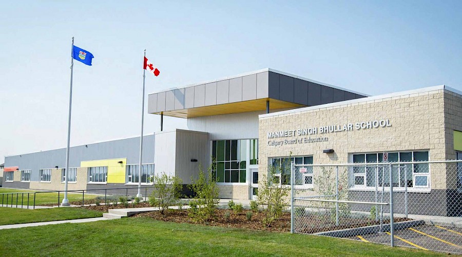A photo of the exterior of Manmeet Singh Bhullar school, with the Albertan and Canadian flag waving in the foreground.