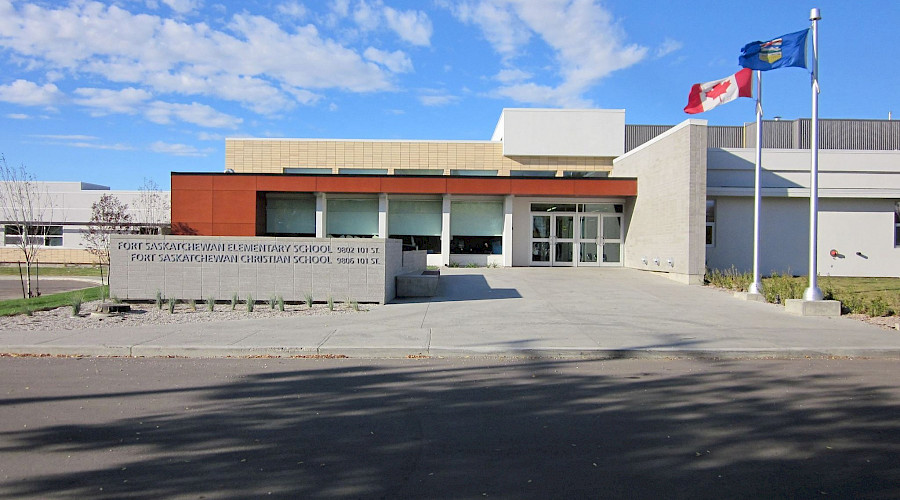 The Alberta and Canada flags waving outside Fort Saskatchewan Elementary school with a cloudy blue sky in the background.