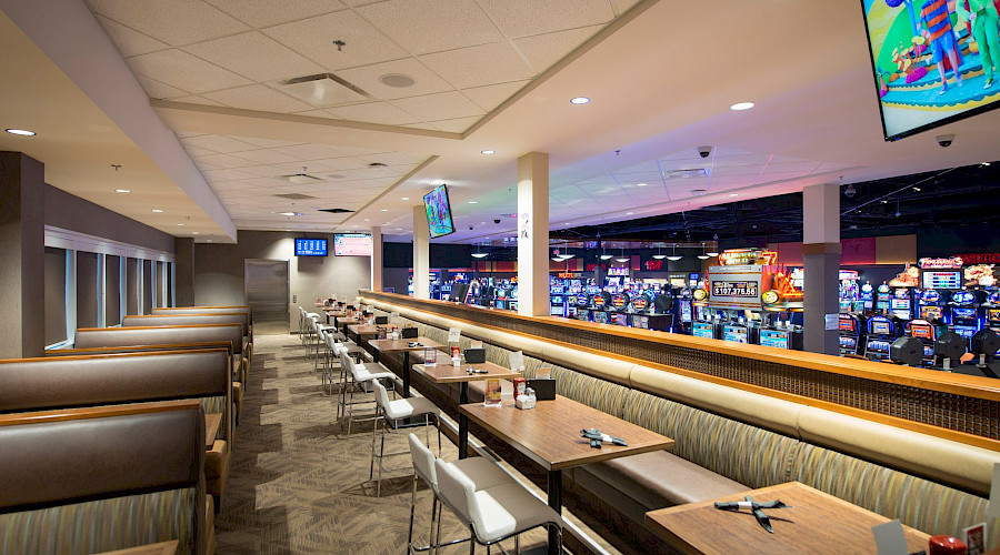 Rows of tables and booths in a casino with multiple VLT machines behind them.