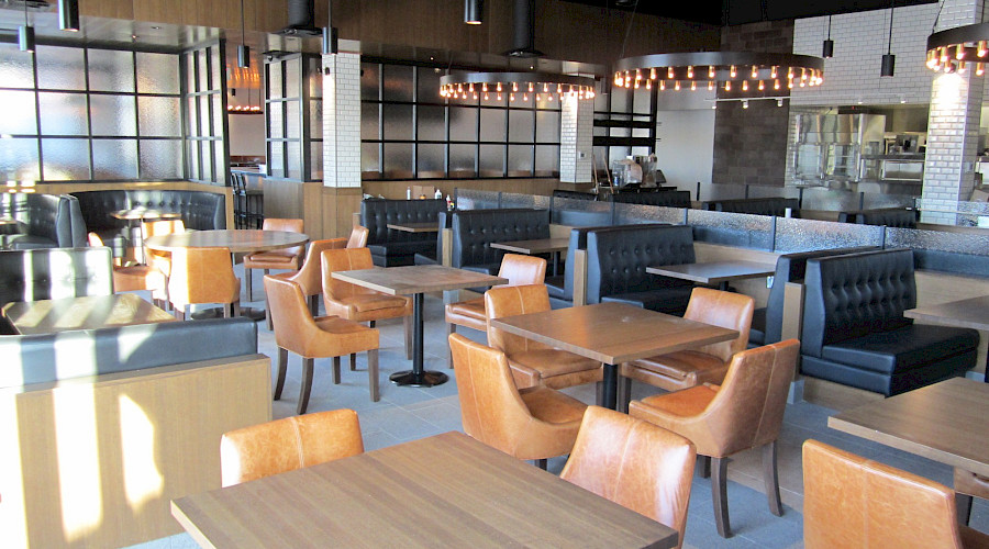 Multiple tables and booths in a restaurant with large, round light fixtures.