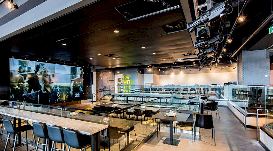 Multiple tables in a large restaurant with a large TV on the entire left wall at the The Cineplex Rec Room project in West Edmonton Mall.
