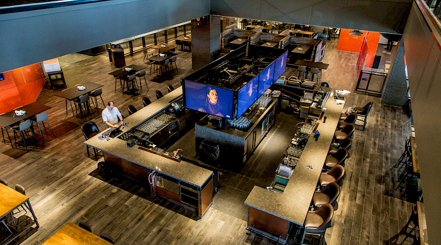 An aerial shot of a large square bar top surrounding multiple large TVs in a dim room at The Cineplex Rec Room project in West Edmonton Mall.