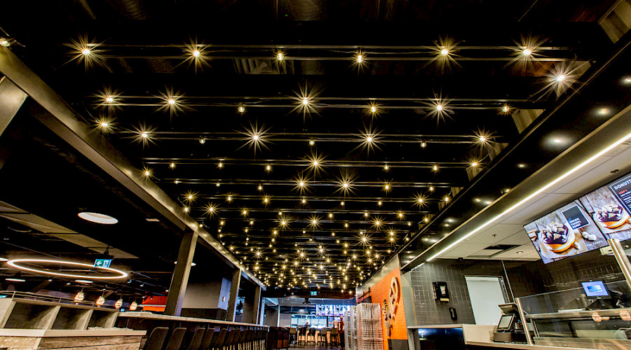 A ceiling with multiple lines of bright yellow pot lights resembling stars at The Cineplex Rec Room project in West Edmonton Mall.
