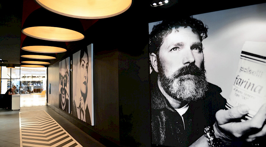 A large black and white canvas print of a man holding a bag of flour in a hallway lined with other prints and round, bright yellow light fixtures at the Double Zero Pizza in Calgary Alberta.