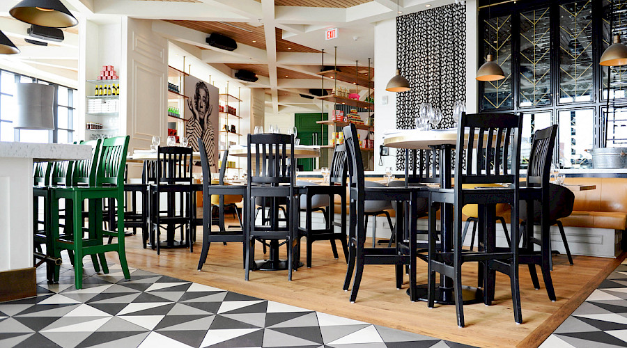 Multiple high top tables in a restaurant with funky tile and hardwood floors, panel wooden ceilings, and pop culture art prints on the walls at the Double Zero Pizza in Calgary, Alberta.