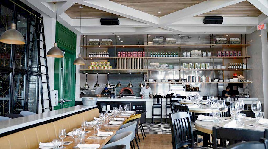 Tables set with wine glasses with a man cooking in an open kitchen with shelves of ingredients in the background at the Double Zero Pizza in Calgary, Alberta.