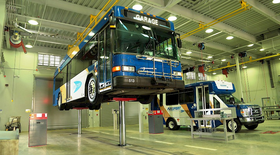 A bus lifted from the ground next to another bus in an autoshop.