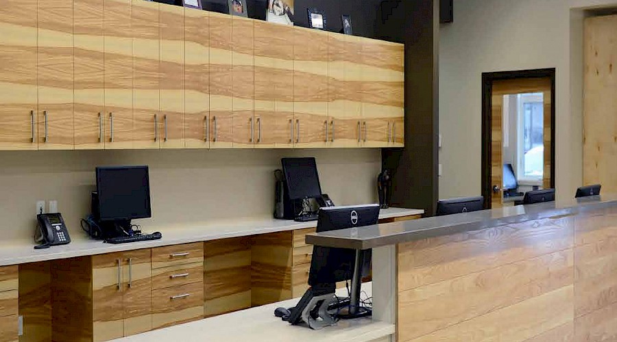 A large reception desk with wooden panelling and cupboards in front of a black wall with high ceilings.