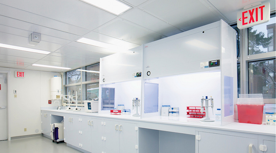 Laboratory equipment on countertops lining the bright white walls inside a laboratory room.