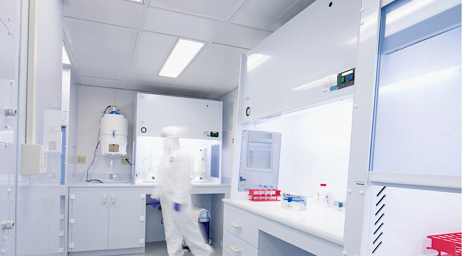 A person in a white hazmat suit walking inside a laboratory room.