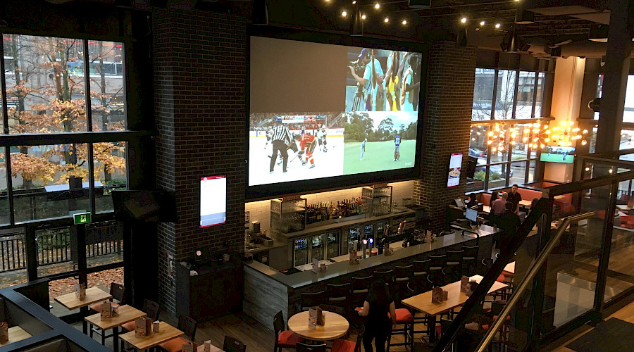 A shot from above of high top tables and a bar top facing a large TV screen in a restaurant.