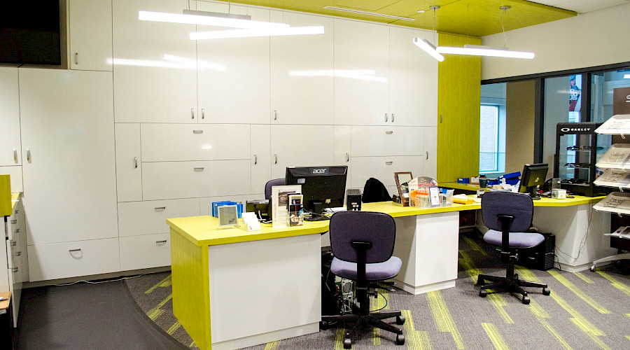 A large desk with multiple chairs in an office with white cupboards on the wall and lime green detailing.