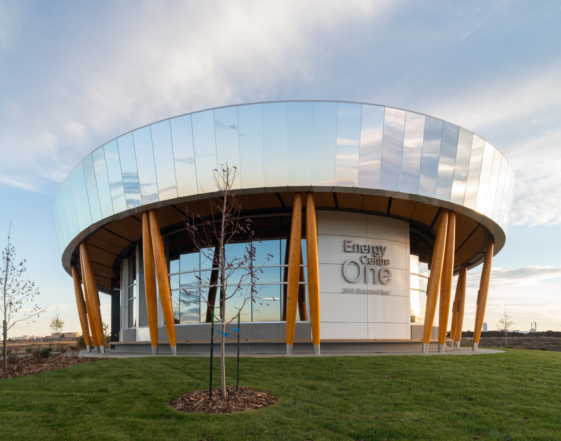 A photo of the Blatchford Energy Centre in Edmonton, with it's mirrored exterior reflecting a cloudy blue sky.