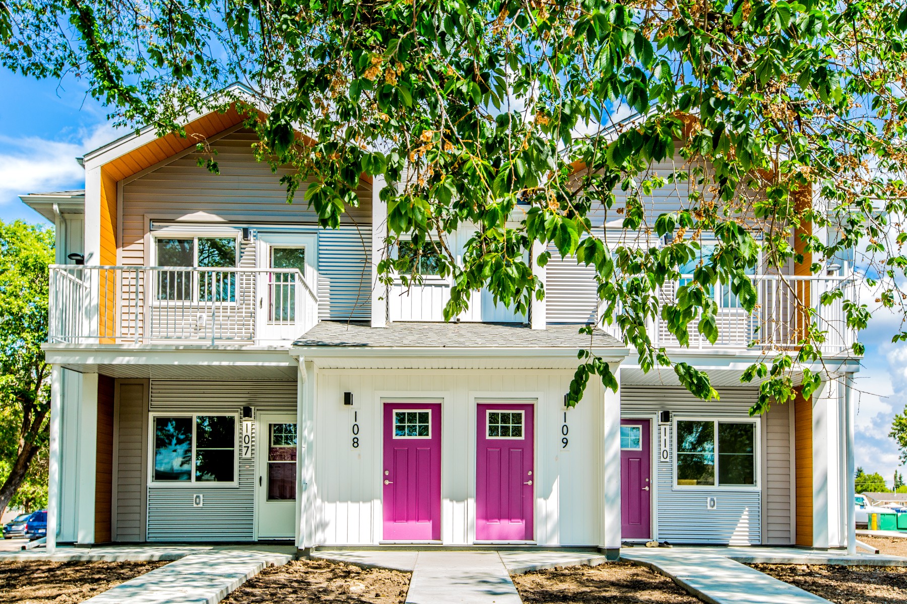 A duplex with two hot pink doors behind multiple tree branches with green leaves.