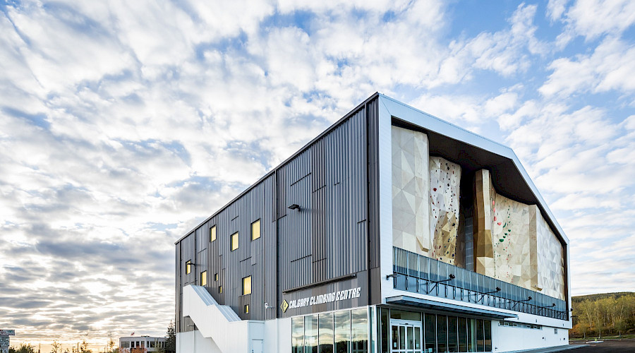 The exterior of the Calgary Climbing Centre, highlighting it's outdoor climbing wall underneath a cloudy blue sky.