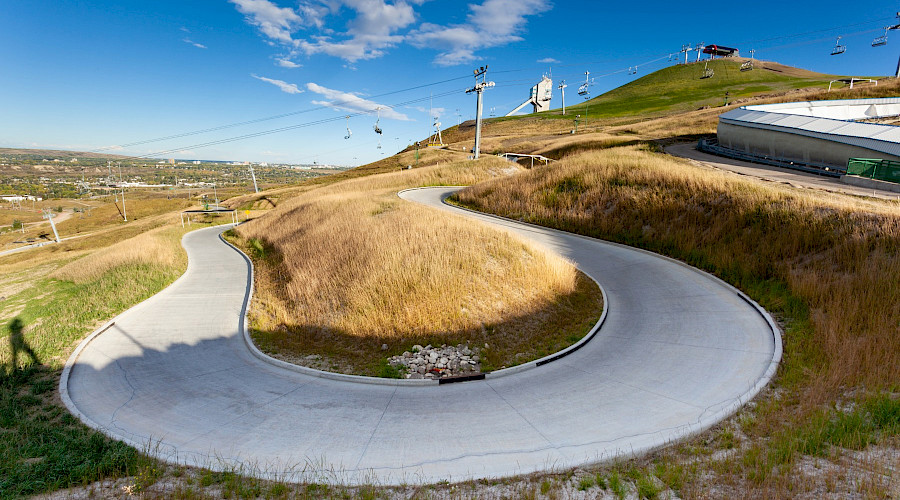 A long curved road in the shape of a U surrounded by yellow grass with a chairlift in the background.