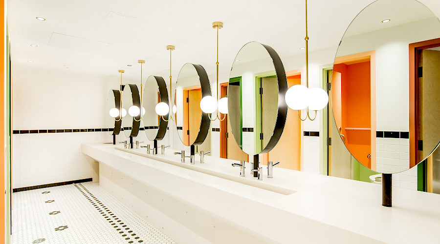 A photo of a long communal sink and six circular mirrors in a bathroom.