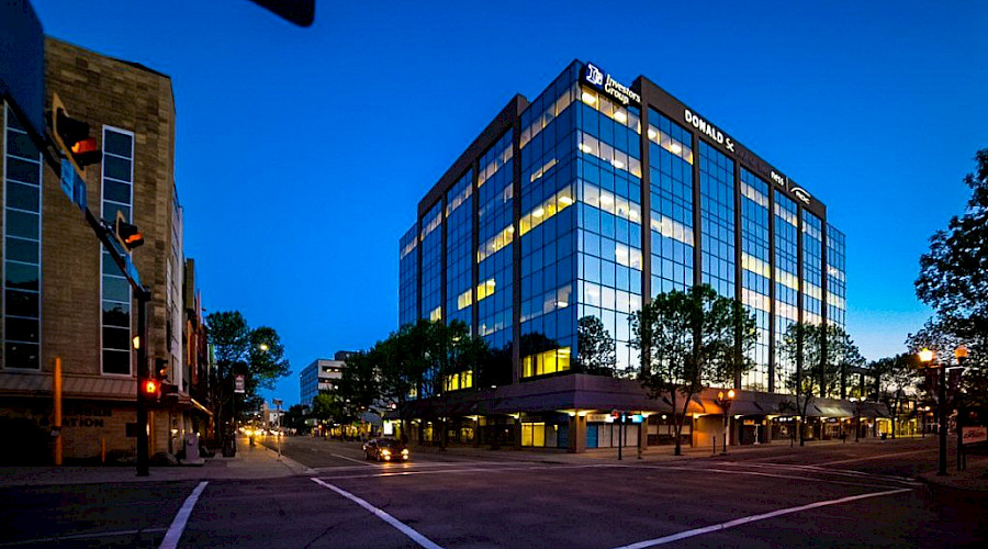 A glass building lit up at night on the corner of a street.