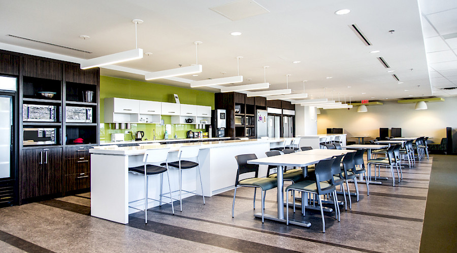 Rows of desks in front of an island in an open kitchen in a large bright room.