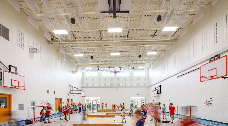 A photo of kids playing floor hockey in a white gymnasium.