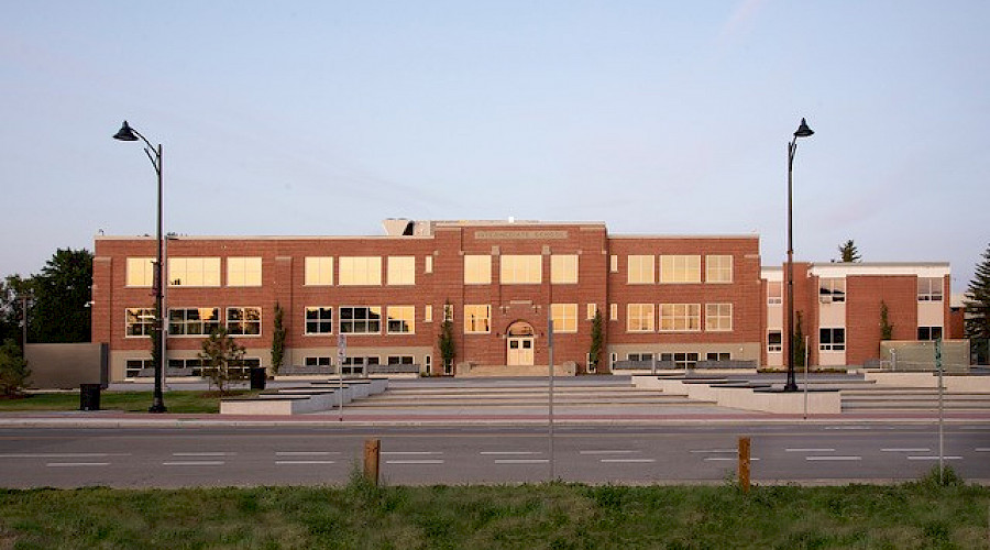 A large brick school behind a road with windows reflecting a sunset.