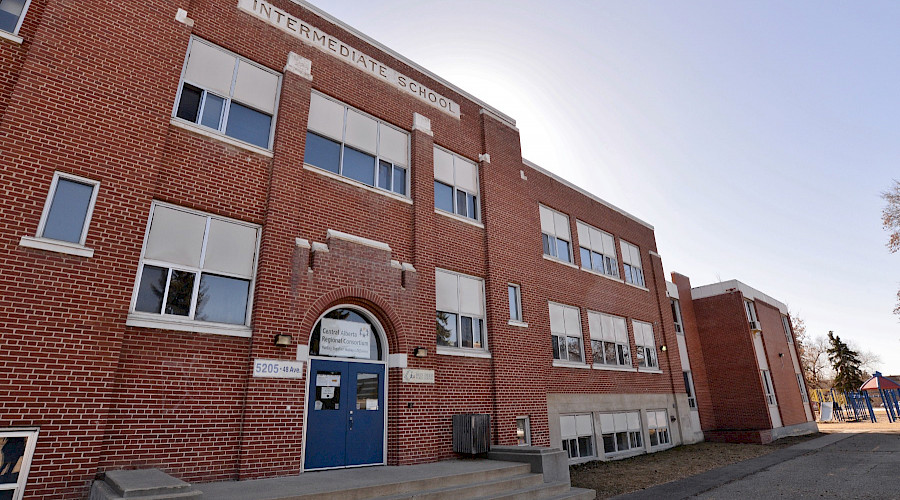 Steps leading up to the blue doors of a large, red brick school.