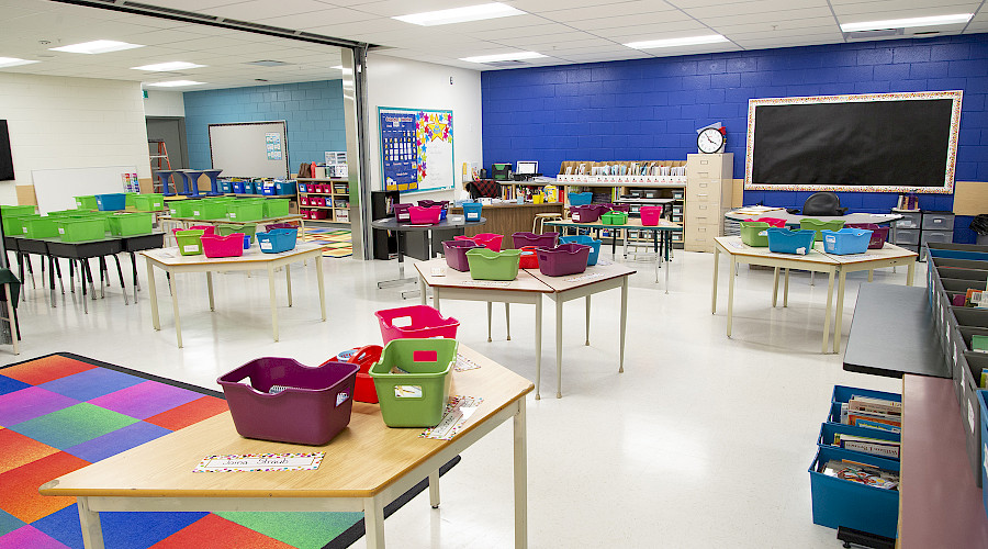 Multicoloured bins on large tables in a blue classroom.