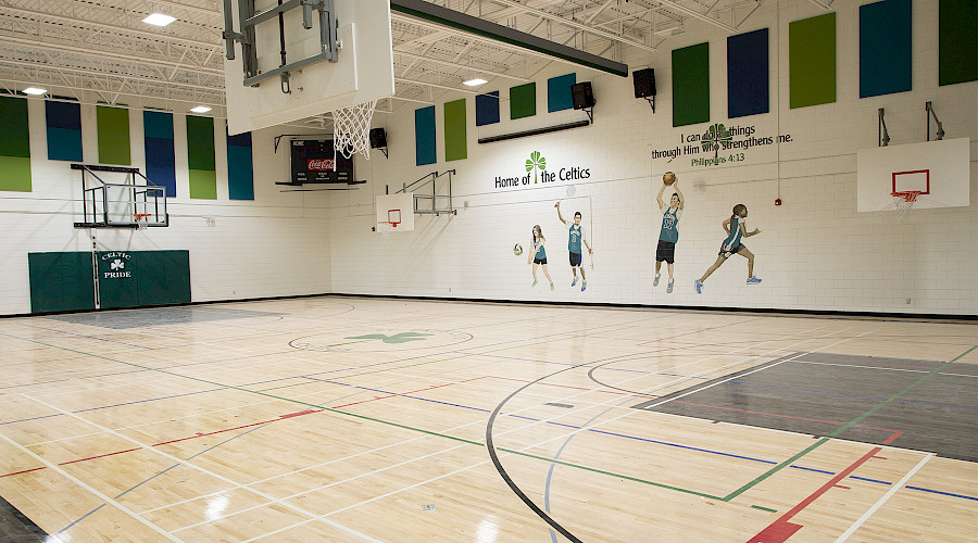 A gymnasium with paintings of kids playing sports on the walls.