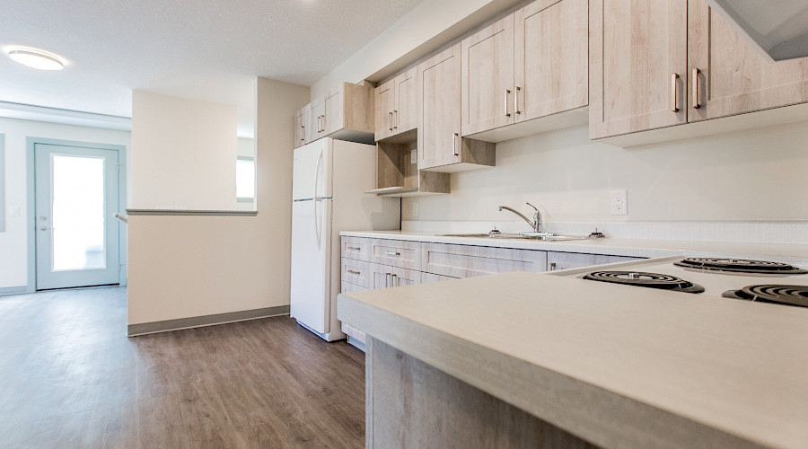 A photo of a kitchen in Linsford Place housing, with light wooden floors and cupboards and sun shining in through the patio door.