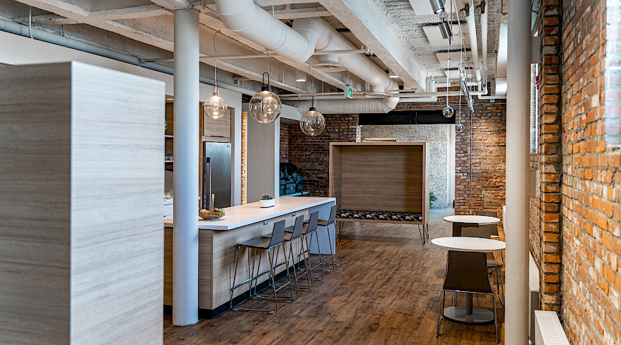 A long kitchen island in a room with an exposed structure ceiling and brick walls.