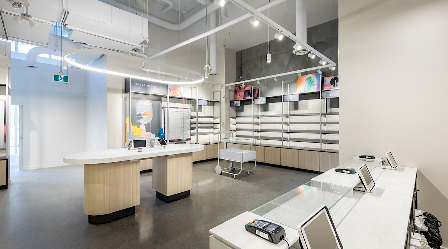 A cashier till facing a small island in a bright room with empty shelves and modern light fixtures.